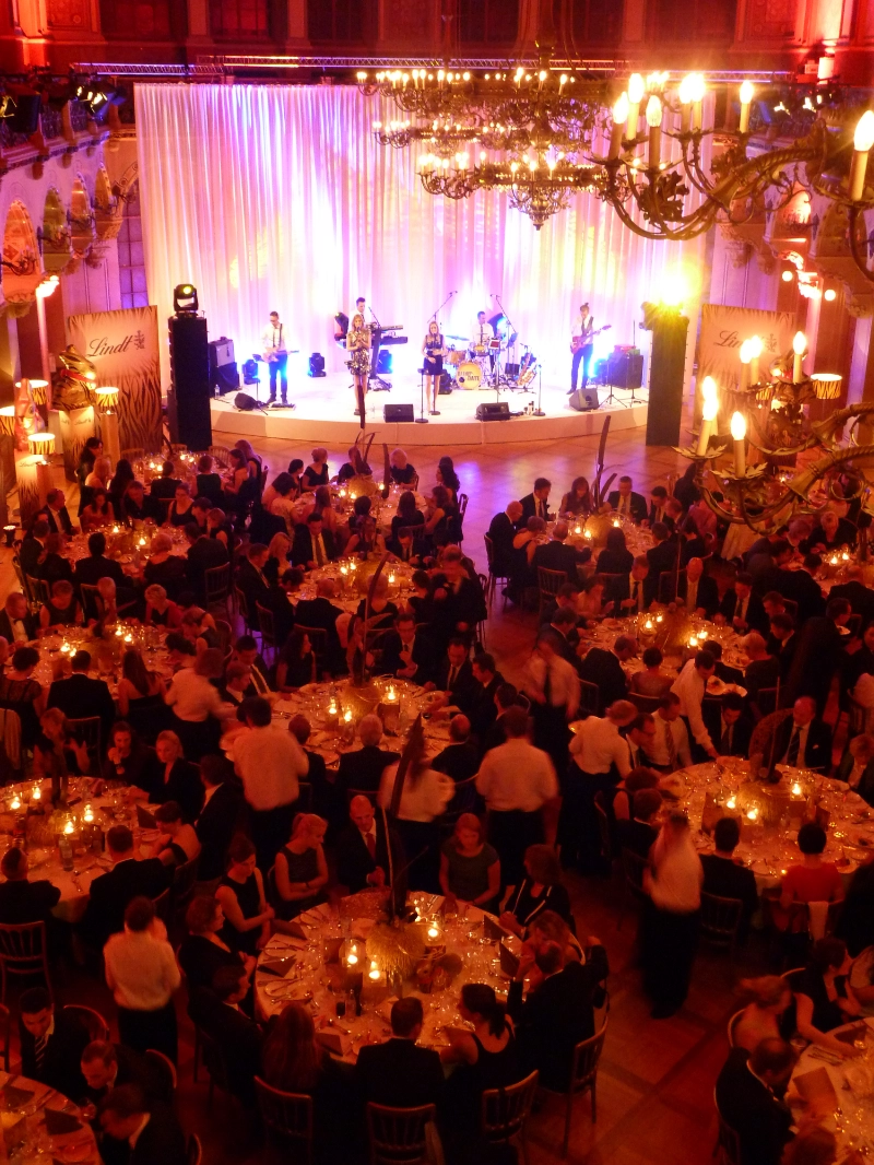 firmenevents Firmenevent Galaabend mit Live Band auf der Bühne und Gästen an runden Tischen.
